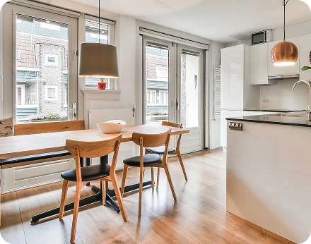 Interior view of a modern apartment dining area and kitchen with light wood flooring, a wooden dining table with black chairs, and white minimalist cabinetry tg renovations