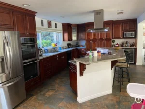 Interior view of an outdated kitchen with dark wood cabinets and mismatched tile flooring before a remodel tg renovations