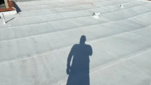 A finished flat roof coated in a bright white reflective sealant by TG Renovations, showing smooth horizontal seams and the shadow of a contractor inspecting the completed work.