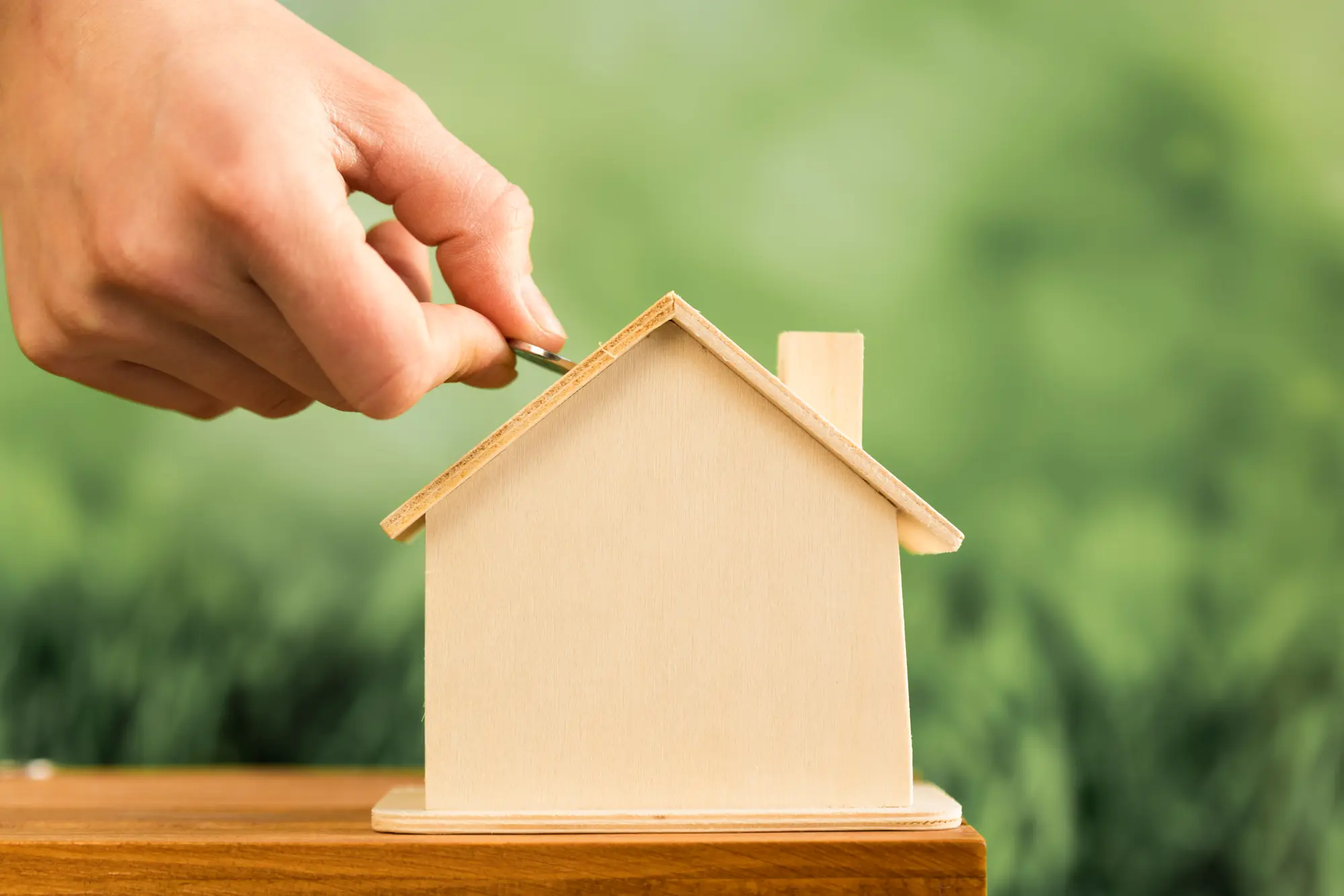 Hand putting a coin into a miniature wooden house representing real estate investment in an in-law suite or ADU built by TG Renovations