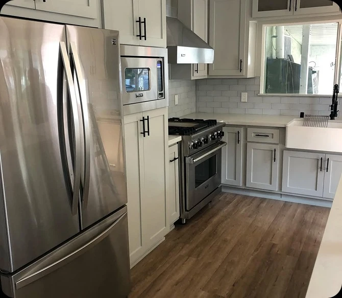 Modern farmhouse kitchen renovation by TG Renovations showcasing light grey shaker cabinets with matte black hardware, a white subway tile backsplash, an apron-front sink, and stainless steel appliances.