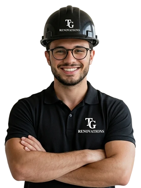 TG Renovations professional contractor: A confident, smiling man wearing glasses, a black polo shirt, and a black hard hat, both featuring the white TG Renovations logo, standing with crossed arms against a black background.
