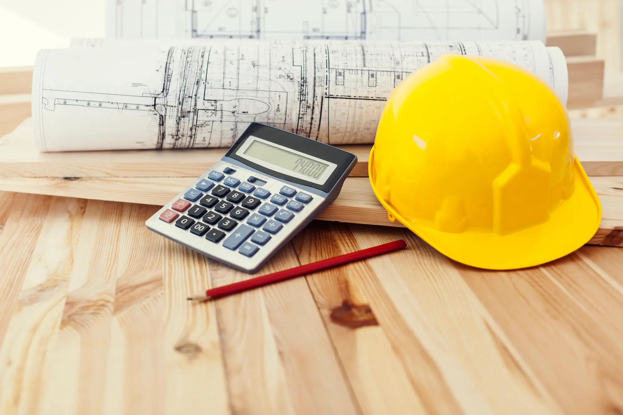 Architectural blueprints, yellow hard hat, and calculator on a wooden desk representing ADU construction loan budgeting – TG Renovations