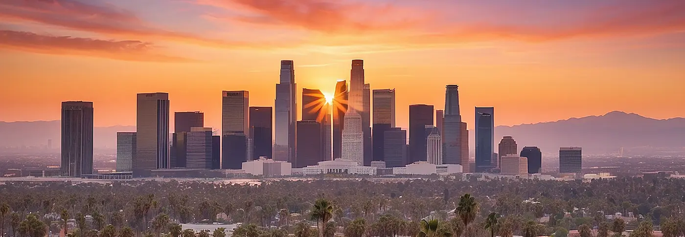 Wide panoramic view of the downtown Los Angeles skyline at sunset with a sunburst between skyscrapers and distant mountains tg renovations