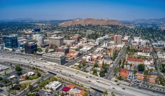 Aerial view of a multi-lane freeway with cars passing through a city in the Inland Empire California under a blue sky with mountains in the background tg renovations