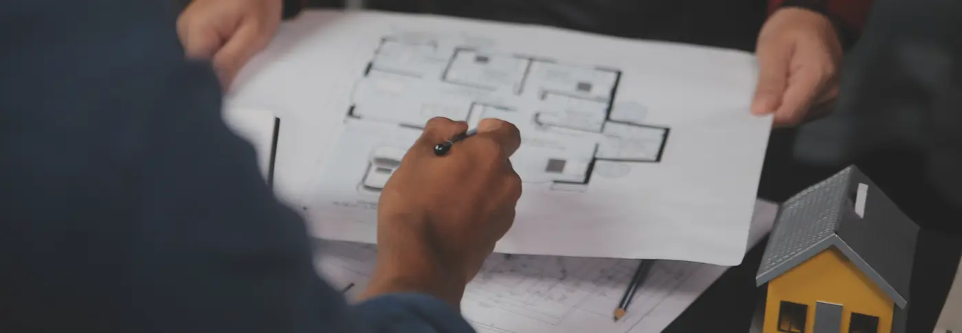 Close up of a construction team reviewing architectural blueprints and a small house model during a project planning meeting tg renovations