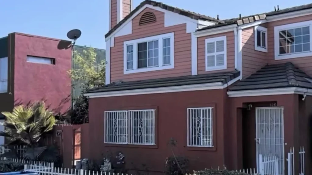 Front view of a two story residential home with faded red stucco and pink siding on a sunny day tg renovations